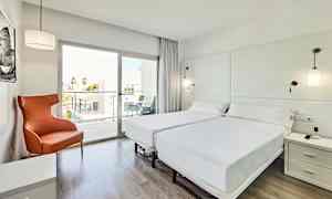 Ett ljust och modernt hotellrum med två enkelsängar, en orange fåtölj och ett glasfönster som leder till en balkong. (AI-genererad text)