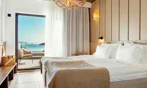 Ett hotellrum med en stor säng och havsutsikt genom en balkongdörr. (AI-genererad text)