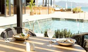 Matbord vid sida av poolen med två rätter och drinkar. (AI-genererad text)