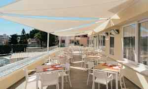 En terrass med bord och stolar under solskyddstak. (AI-genererad text)