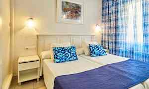 Bild av sovrum med två enkelsängar, blå kudde och täcke, samt blå gardiner. (AI-genererad text)