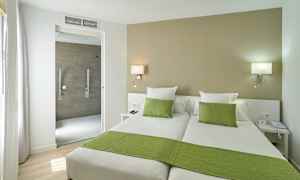 Hotellrum med två enkelsängar, gröna sängkläder och en öppning mot badrummet. (AI-genererad text)