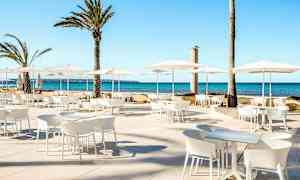 Utomhus sittgrupp med vita möbler och parasoller, samt palmer i bakgrunden vid havet. (AI-genererad text)