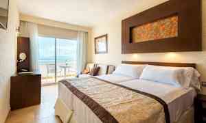 Ett hotellrum med dubbelsäng, ett skrivbord och en balkong med utsikt. (AI-genererad text)