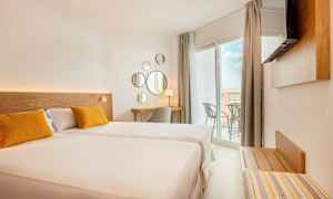 Ett ljust hotellrum med en stor säng, två gula kuddar, en skrivbordshörna och en balkong med utsikt. (AI-genererad text)