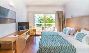 Hotellrum med två bäddar, skrivbord, och fönster med utsikt mot balkong. (AI-genererad text)