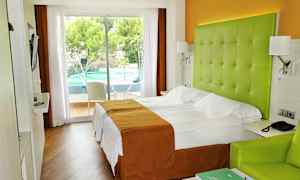 Hotellrum med dubbelsäng, grönt huvudgavel och utsikt till en utomhuspool. (AI-genererad text)