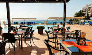 Uteservering med bord och stolar nära pool och hav. (AI-genererad text)