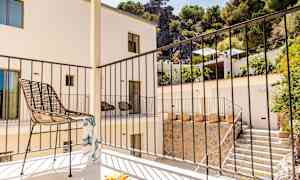 En balkong med en stol och ett räcke, omgiven av en byggnad och grönska. (AI-genererad text)