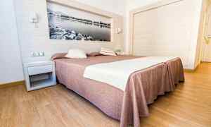 Hotellrum med en stor säng täckt av ett brunaktigt sängöverkast och vita lakan, med trägolv och en väggdekoration i form av en svartvit bild. (AI-genererad text)