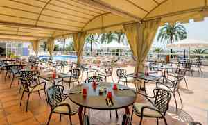 En restaurang uteplats med tak, där bord och stolar är uppställda kring en pool. (AI-genererad text)