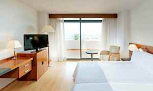 Ett hotellrum med två sängar, en tv på en träbyrå och en glasdörr som leder ut till en terrass. (AI-genererad text)