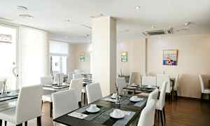 Ett ljust restaurangutrymme med vita stolar och mörka bord, dukade med porslin och dekorationer. (AI-genererad text)