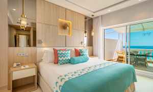 Hotellrum med dubbelsäng, dekorerad i blått och vitt, med utsikt över havet från en balkong. (AI-genererad text)