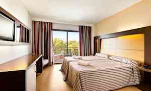 Två sängar i ett hotellrum med randiga överkast, en balkong med utsikt och en arbetsyta. (AI-genererad text)