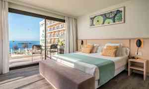 Hotellrum med säng, sittmöbler och en utsikt mot havet genom stora fönster. (AI-genererad text)