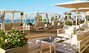 Loungeområde med sittgrupper och solbäddar under parasoller, samt havsutsikt. (AI-genererad text)