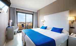 Ett hotellrum med en dubbelsäng, ljusa väggar och blå sängkläder. (AI-genererad text)