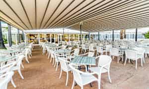 En utomhusrestaurang med många vita bord och stolar under ett tak. (AI-genererad text)