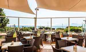 Bild på en utomhusterrass med bord, stolar och havsutsikt. (AI-genererad text)