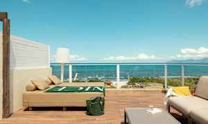 Terrass med modern möblering och utsikt över havet, inklusive en solbädd, soffmöbler och bord. (AI-genererad text)