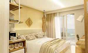 Ett hotellrum med en dubbelsäng, ljus inredning och ett fönster som vetter mot en balkong. (AI-genererad text)