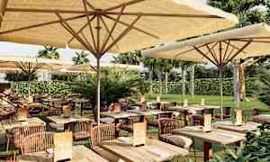 En utomhusrestaurang med bord och stolar under parasoller, omgiven av grönska. (AI-genererad text)