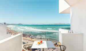 Utsikt från en balkong mot en strand med turkost vatten, sand och människor som badar. (AI-genererad text)