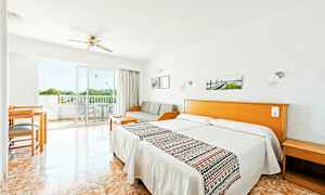 Ett hotellrum med ljus inredning, två enkelsängar, en soffa, ett bord och stolar samt en balkong med utsikt. (AI-genererad text)