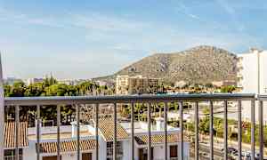 Utsikt från en balkong över byggnader med tegelpannor och omgivande stadslandskap, med ett berg i bakgrunden. (AI-genererad text)