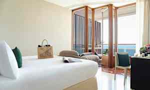 Ett hotellrum med en säng, skrivbord med stol, och en balkong med utsikt över havet. (AI-genererad text)