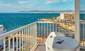 Utsikt från en balkong mot en kust med hav och byggnader i bakgrunden. (AI-genererad text)