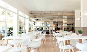 Ljus och modern restaurang med vita möbler och gröna växter. (AI-genererad text)