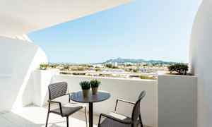 Balkong med bord och stolar, utsikt över omgivande byggnader och berg. (AI-genererad text)