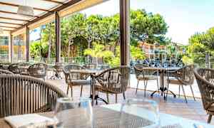 Utomhus sittområde med bord och stolar, omgiven av gröna träd och en byggnad i bakgrunden. (AI-genererad text)