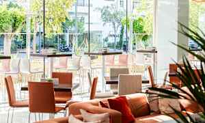 Ett ljus och modern sittområde med bord och stolar, samt stora fönster som erbjuder utsikt över grönskan utanför. (AI-genererad text)