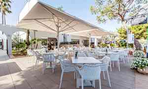 En utomhusrestaurang med vita bord och stolar samt stora parasoller. (AI-genererad text)