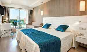 Hotellrum med två sängar, en soffa och en glasbalkong. (AI-genererad text)