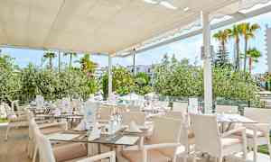 Restaurang med vita möbler och tak, omgiven av grönska. (AI-genererad text)