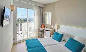 Ett ljust hotellrum med två sängar, blåa kuddar och överkast, samt en balkong med utsikt. (AI-genererad text)