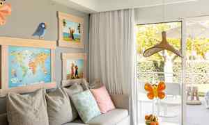 Ett rum med en soffa, kuddar, tavlor samt ett bord med en skål med frukt framför en balkongdörr. (AI-genererad text)