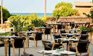 Utomhusrestaurang med bord och stolar samt gröna växter. (AI-genererad text)