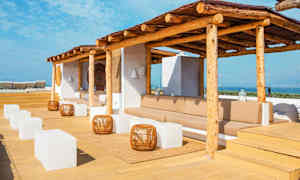 Terrass med solskydd av trä, sittplatser, vita kubformade bord och utsikt över havet. (AI-genererad text)