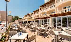 Terrassrestaurang med bord och stolar, omgiven av en byggnad med balkonger. (AI-genererad text)