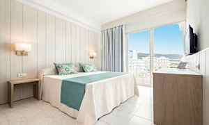 Ett ljust hotellrum med en dubbelsäng klädd i vit och turkos bäddning, två sängbord, en garderob och en balkong med utsikt över staden. (AI-genererad text)