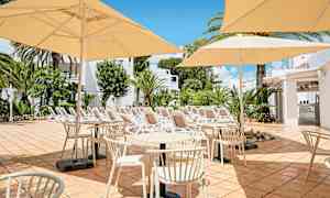 Bild av en terrass med bord, stolar och parasoller i en solig miljö. I bakgrunden syns solstolar och grönska. (AI-genererad text)