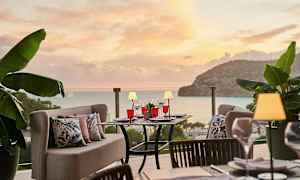 Uteservering med bord och soffor, omgiven av grön växtlighet, med utsikt över havet under en solnedgång. (AI-genererad text)