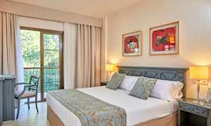 Ett hotellrum med en dubbelsäng, nattduksbord, två bordlampor och en stol vid ett skrivbord. Bakom sängen hänger två tavlor på väggen. (AI-genererad text)