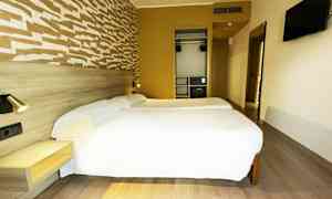 Ett hotellrum med två enkelsängar, en väggmonterad TV och en garderob. (AI-genererad text)