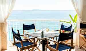 Utsikt över ett dukat bord med blå stolar och hav i bakgrunden. (AI-genererad text)